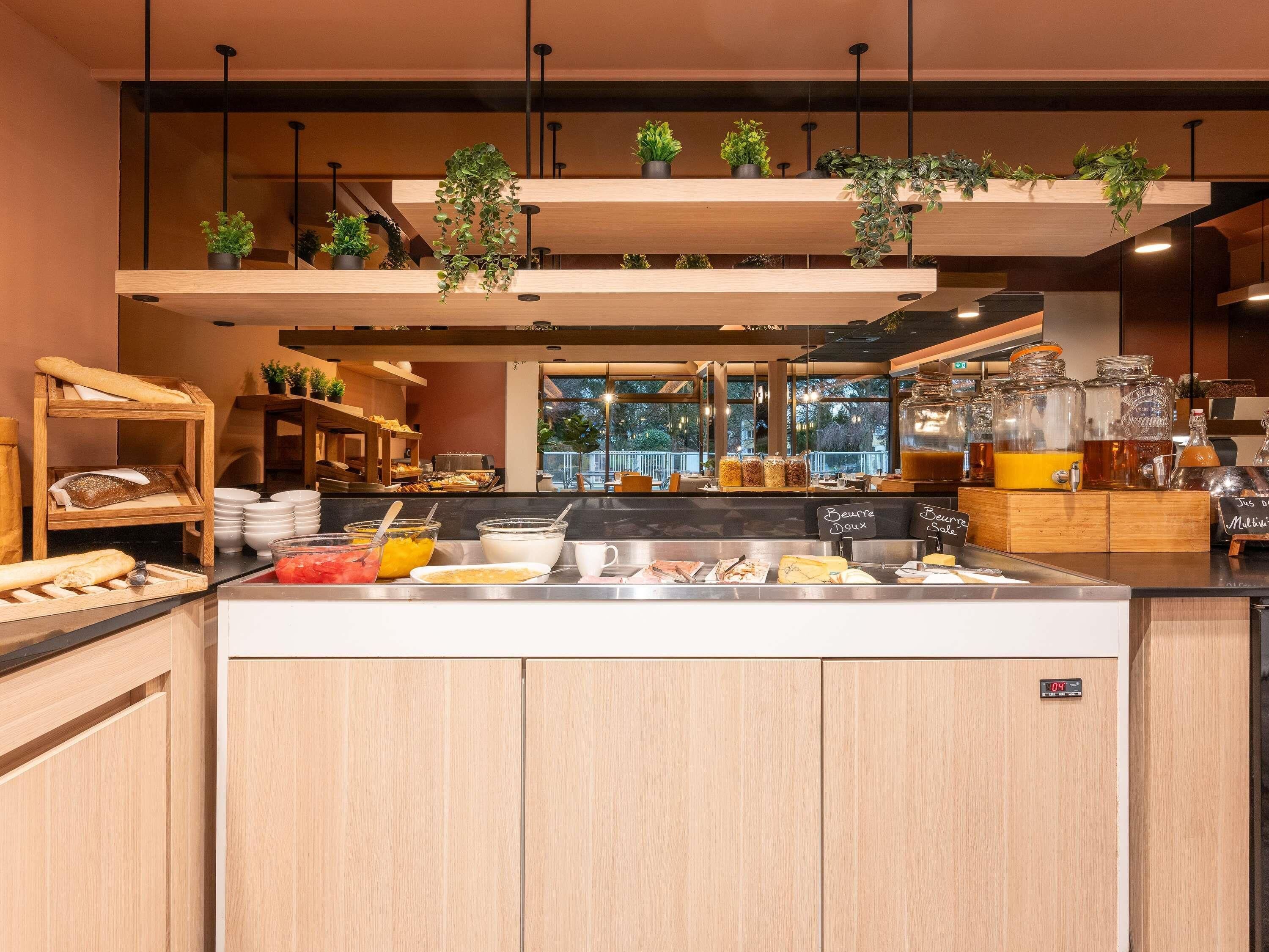 A breakfast buffet with various food items, a coffee station, and hanging plants.