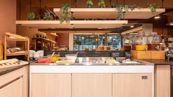 A breakfast buffet with various food items, a coffee station, and hanging plants.