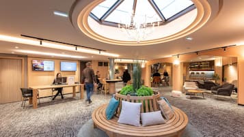 A modern hotel lobby with a central wooden seating area, a bar, and a skylight.