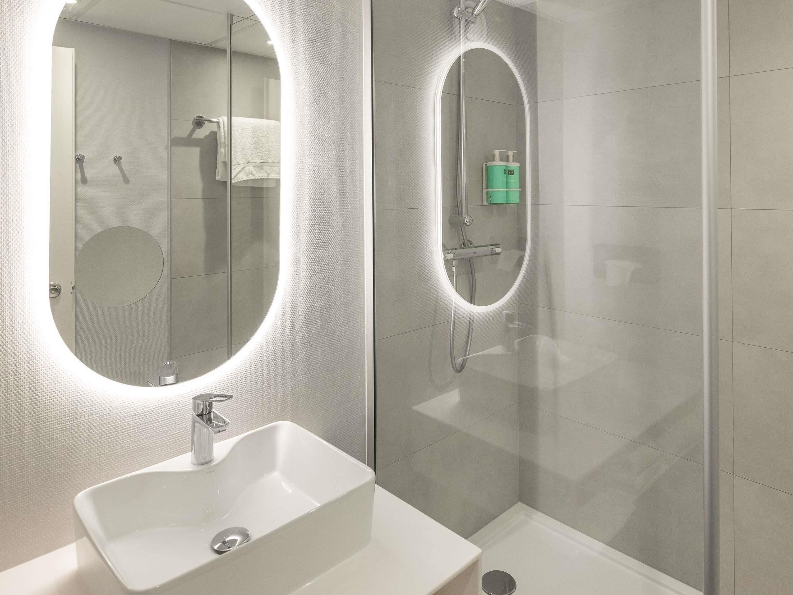 Un bany modern amb un mirall gran, un lavabo i una dutxa.