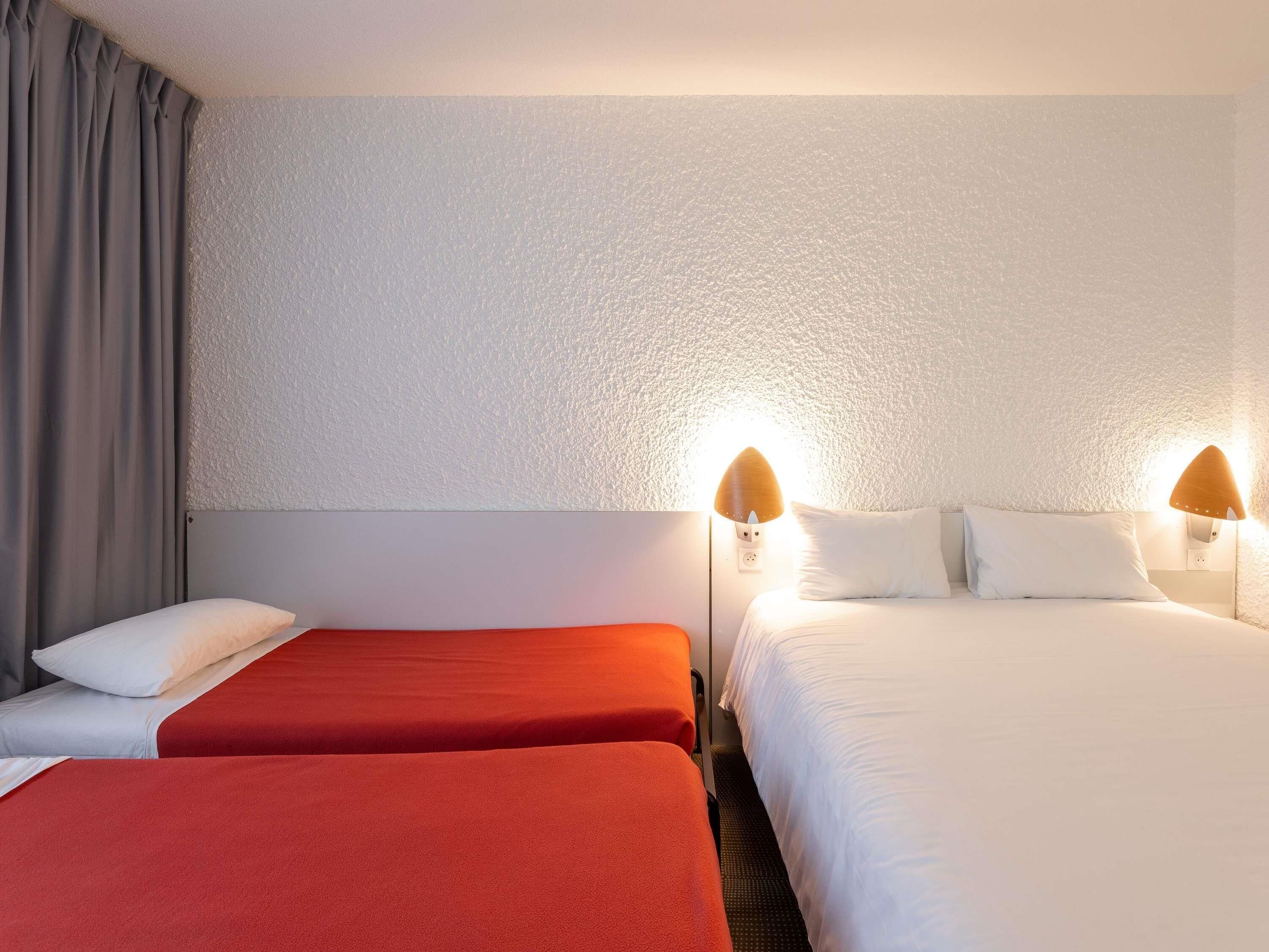 Habitación de hotel con dos camas, una cortina gris y una pared con textura.