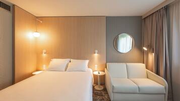 A hotel room with a bed, a sofa, a round mirror, and two wall-mounted lamps.