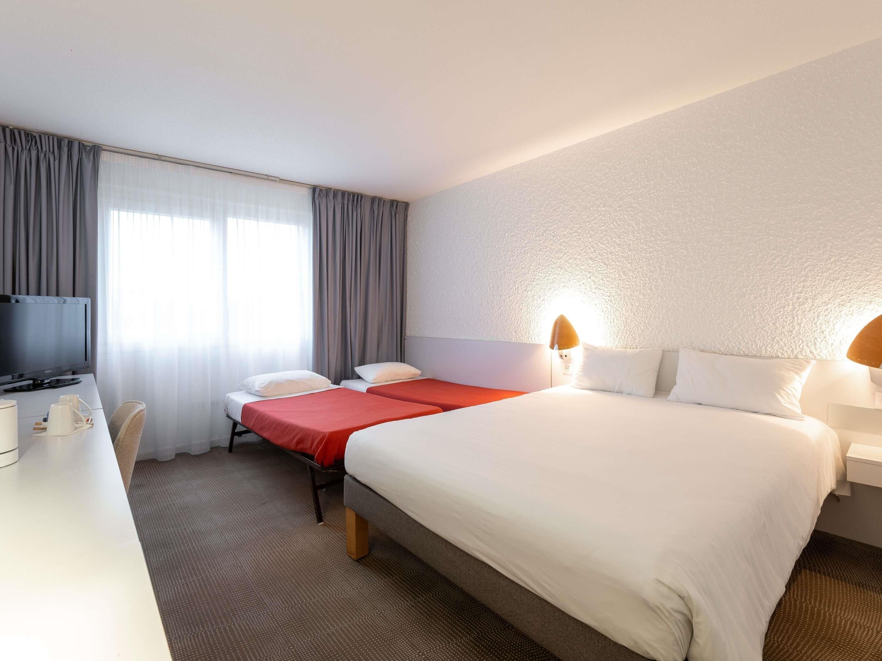 A hotel room with a bed, a desk, a television, and a window with curtains.