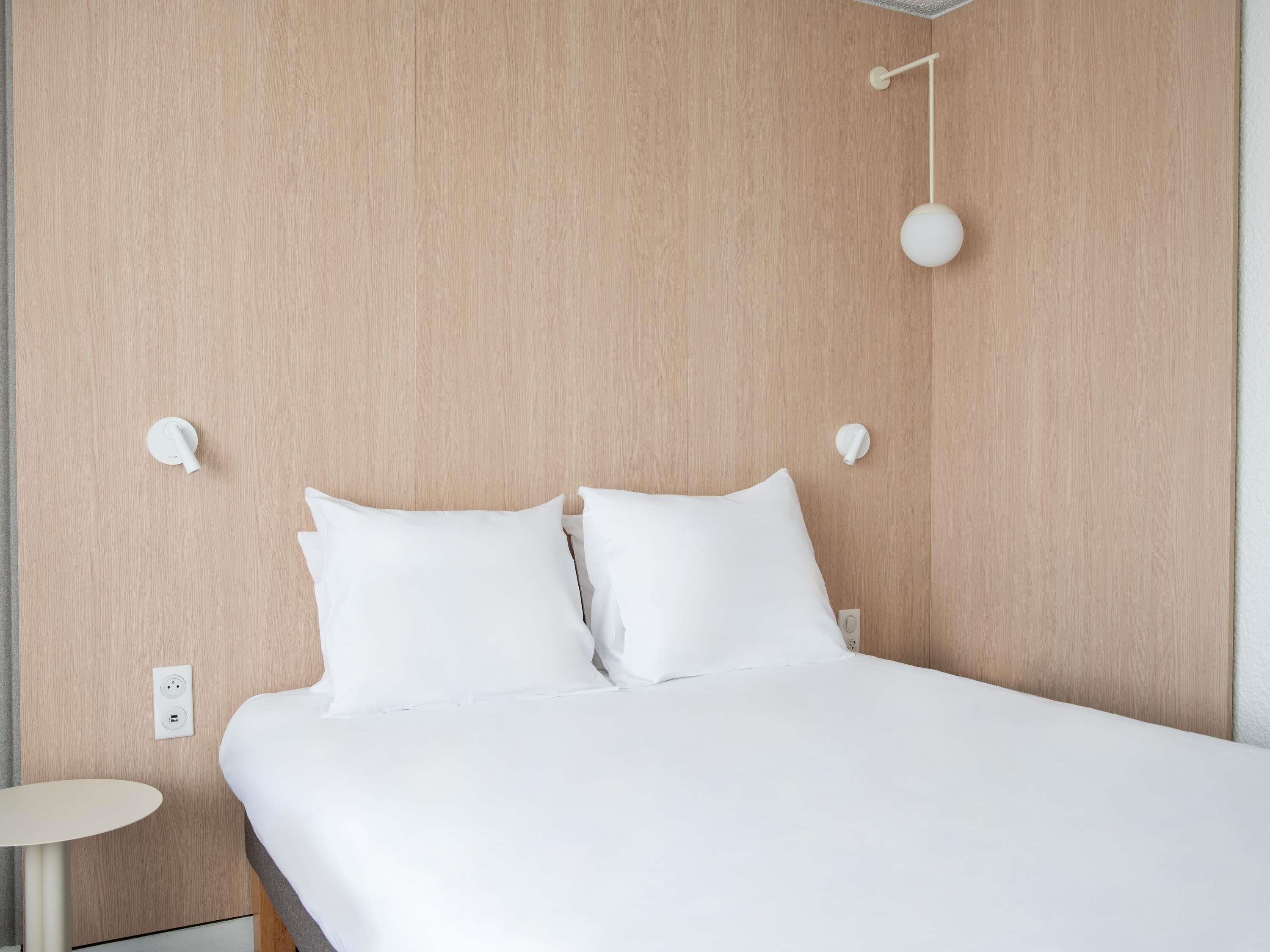 Ein ordentlich bezogenes Bett mit weißen Leinen in einem Zimmer mit Holzwandverkleidung und einem kleinen runden Tisch daneben.