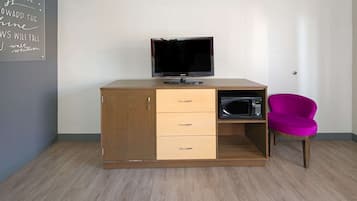 Un escritorio de madera con un televisor de pantalla plana, un microondas y una silla rosa.
