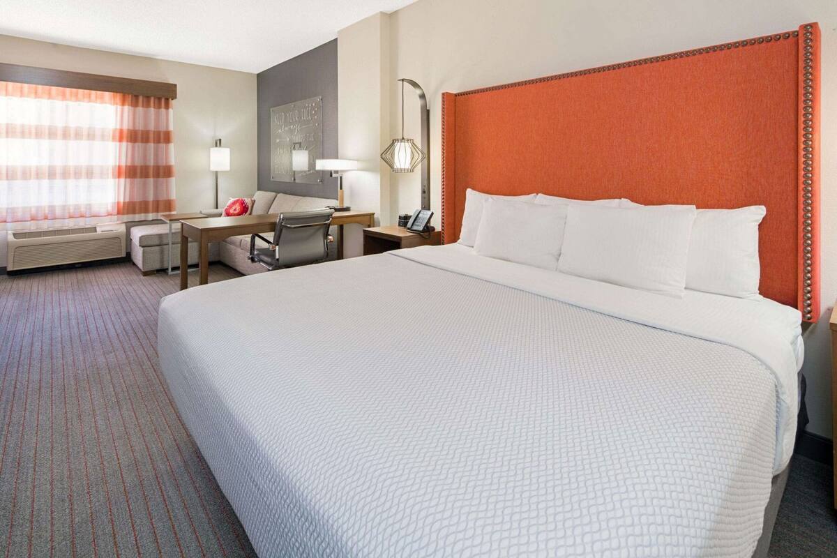 Hotelkamer met een groot bed, een bureau, een stoel, een lamp en een kunstwerk aan de muur.