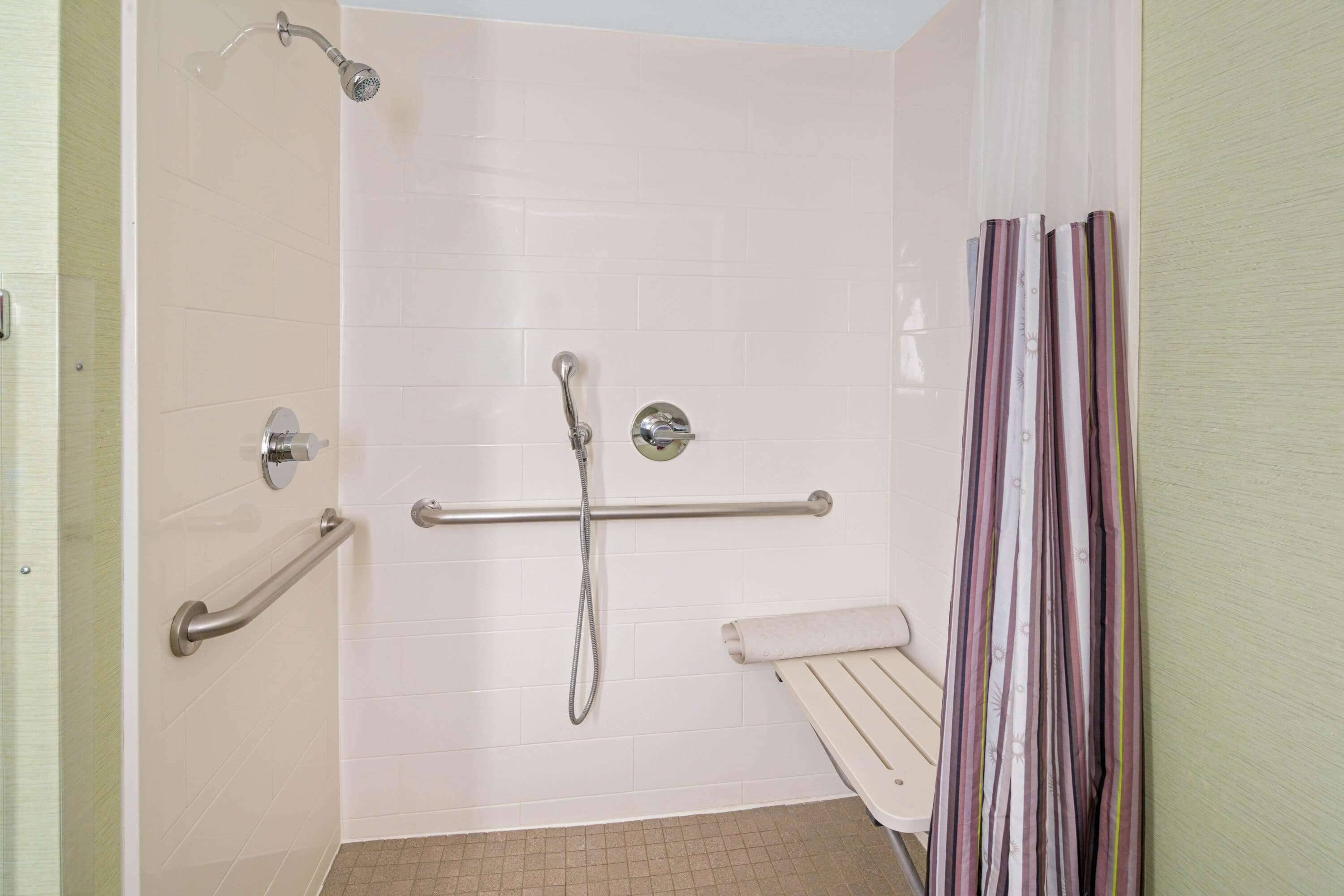 A bathroom with a shower, grab bars, a towel rack, and a striped curtain.