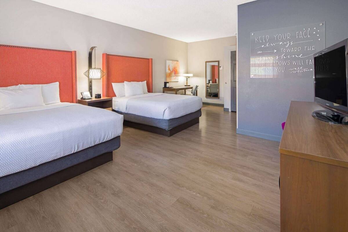 Een hotelkamer met twee bedden, een televisie, een bureau en een motiverende quote op de muur.
