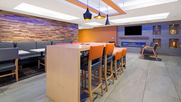Een moderne bar met een houten toonbank, oranje barstoelen en een flatscreen aan de muur.