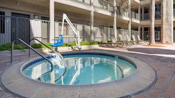 A swimming pool with a blue interior, surrounded by a paved area with lounge chairs and a metal railing.