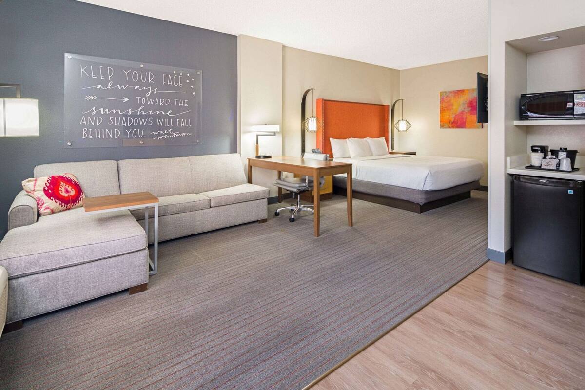 Hotelkamer met een slaapbank, een bed, een bureau, een klein tafeltje, een aan de muur bevestigde televisie, een magnetron en een koelkast.