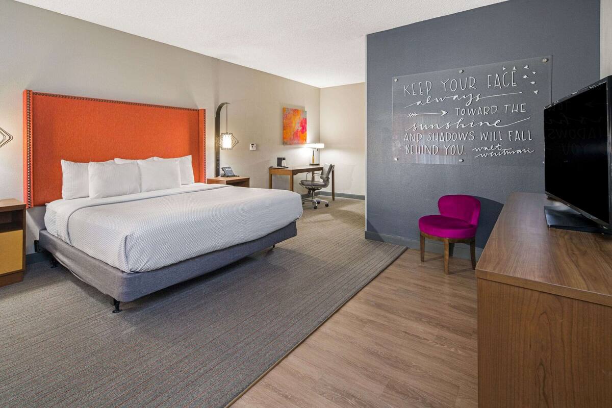 Een hotelkamer met een bed, een bureau, een stoel, een televisie en een motiverende quote op de muur.