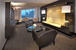 Een moderne hotelkamer met een groot raam, een bank, twee fauteuils, een salontafel en een televisie.