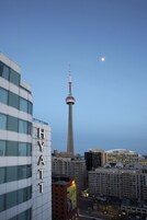 A high-rise building with the word "HYATT" on its facade, a prominent tower in the background, and a clear sky.