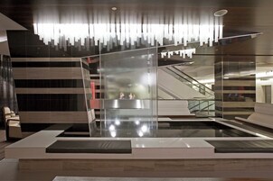 Een moderne lobby met een receptiebalie, een glazen scheidingswand en een roltrap.