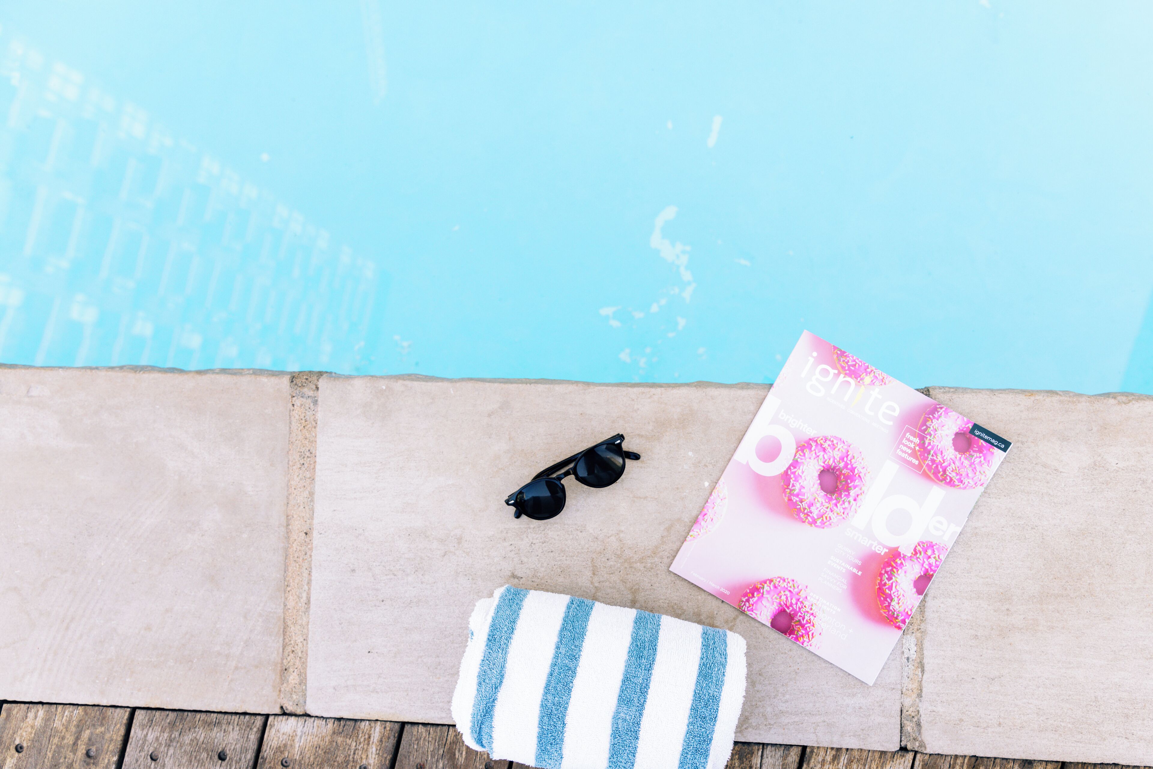 Ein Poolbereich mit blauem Pool, einer Sonnenbrille, einem gestreiften Handtuch und einer Zeitschrift.