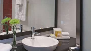 A modern bathroom with a large mirror, white sink, and a vase with green plants.