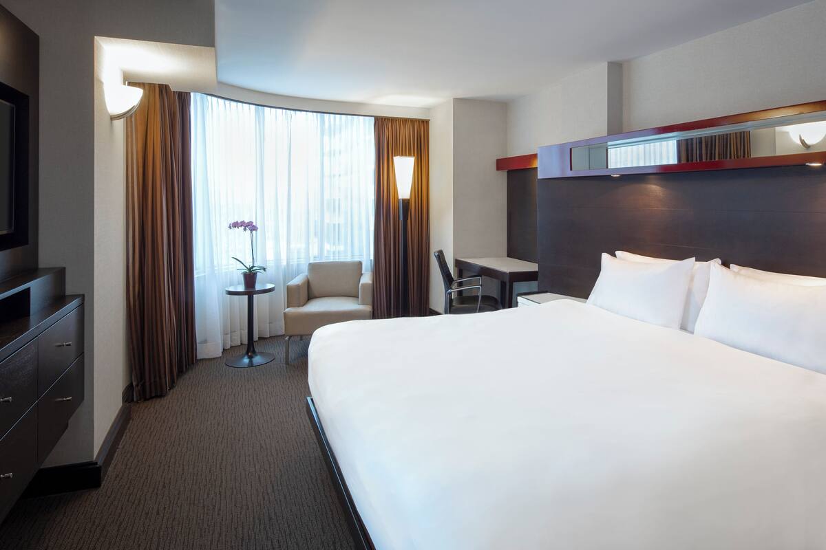 A hotel room with a large bed, a desk, a chair, a TV, and a window with curtains.