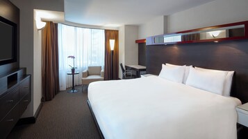 A hotel room with a large bed, a desk, a chair, a TV, and a window with curtains.