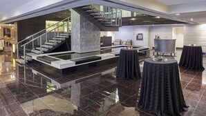 A spacious, modern interior with a central staircase, a seating area with round tables, and a bar.