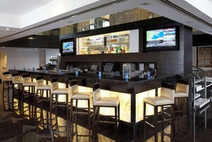 Een moderne barruimte met een marmeren aanrecht, meerdere barkrukken en twee televisies boven de bar.
