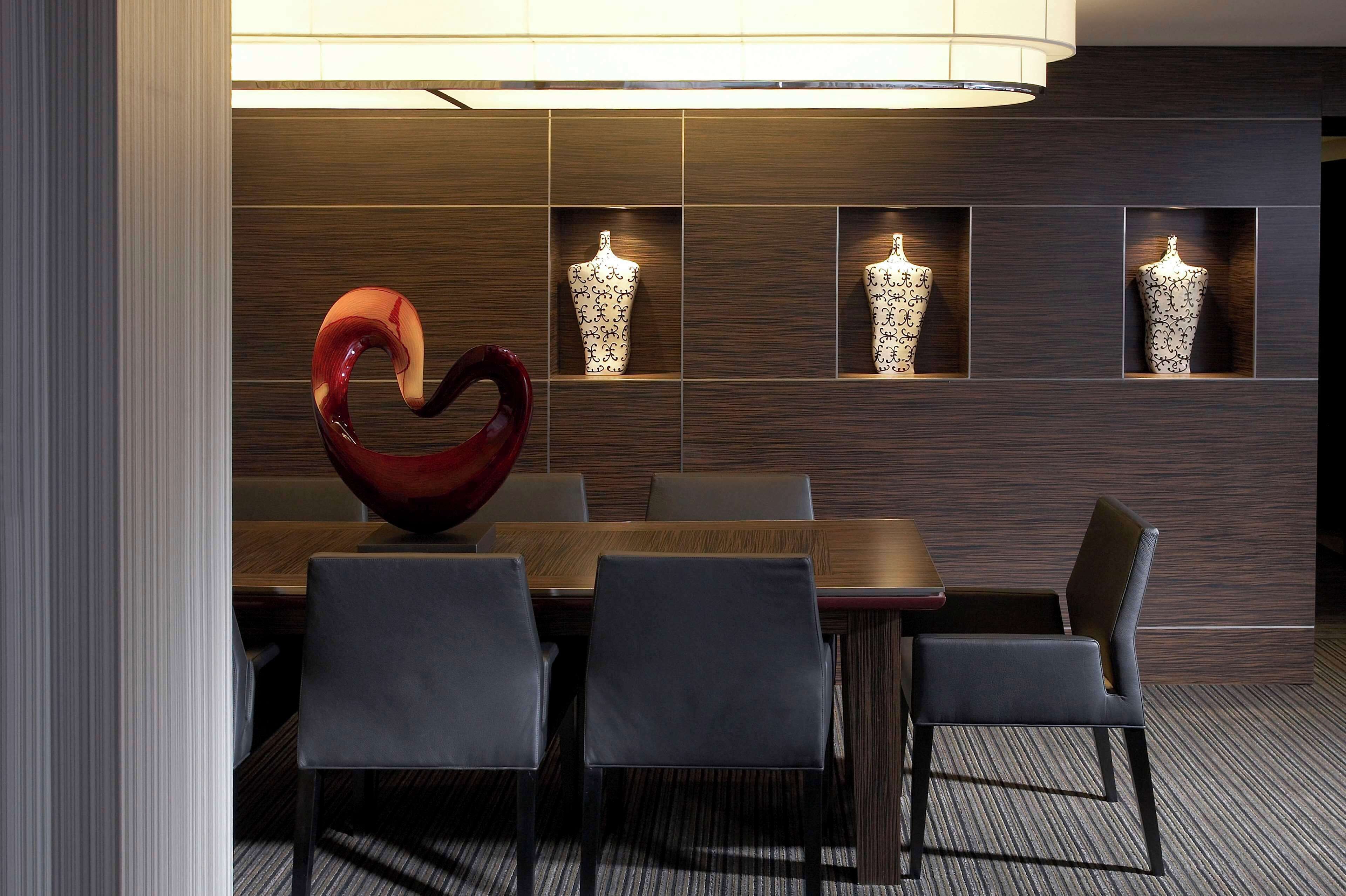 Un espace de salle à manger moderne avec une table en bois et des chaises noires, une sculpture abstraite rouge et des vases décoratifs accrochés au mur.