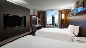 A hotel room with two beds, a desk, a TV, and a view of a cityscape.