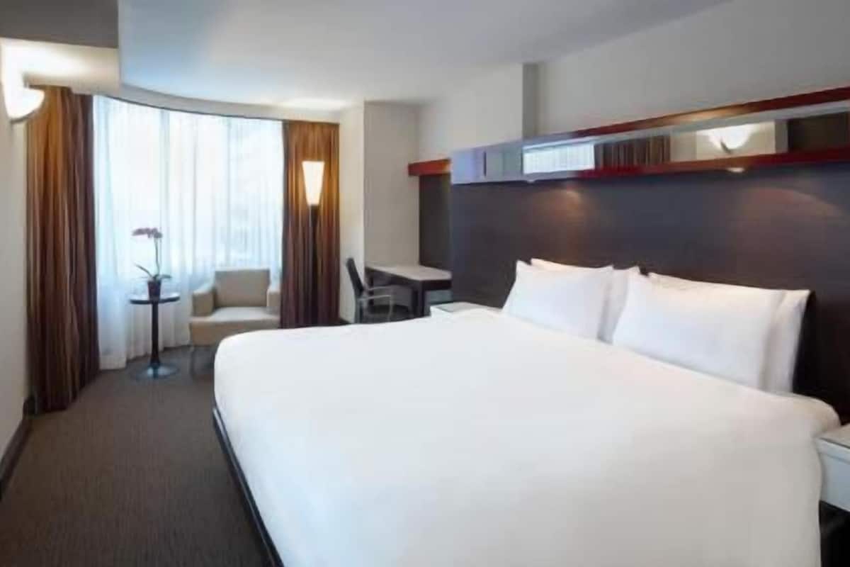 A hotel room with a large bed, a TV, a desk, and a chair.