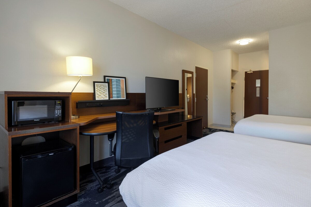 A hotel room with a bed, a desk with a computer, a microwave, and a small refrigerator.