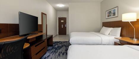 A hotel room with a TV, two beds, a desk, and a lamp.