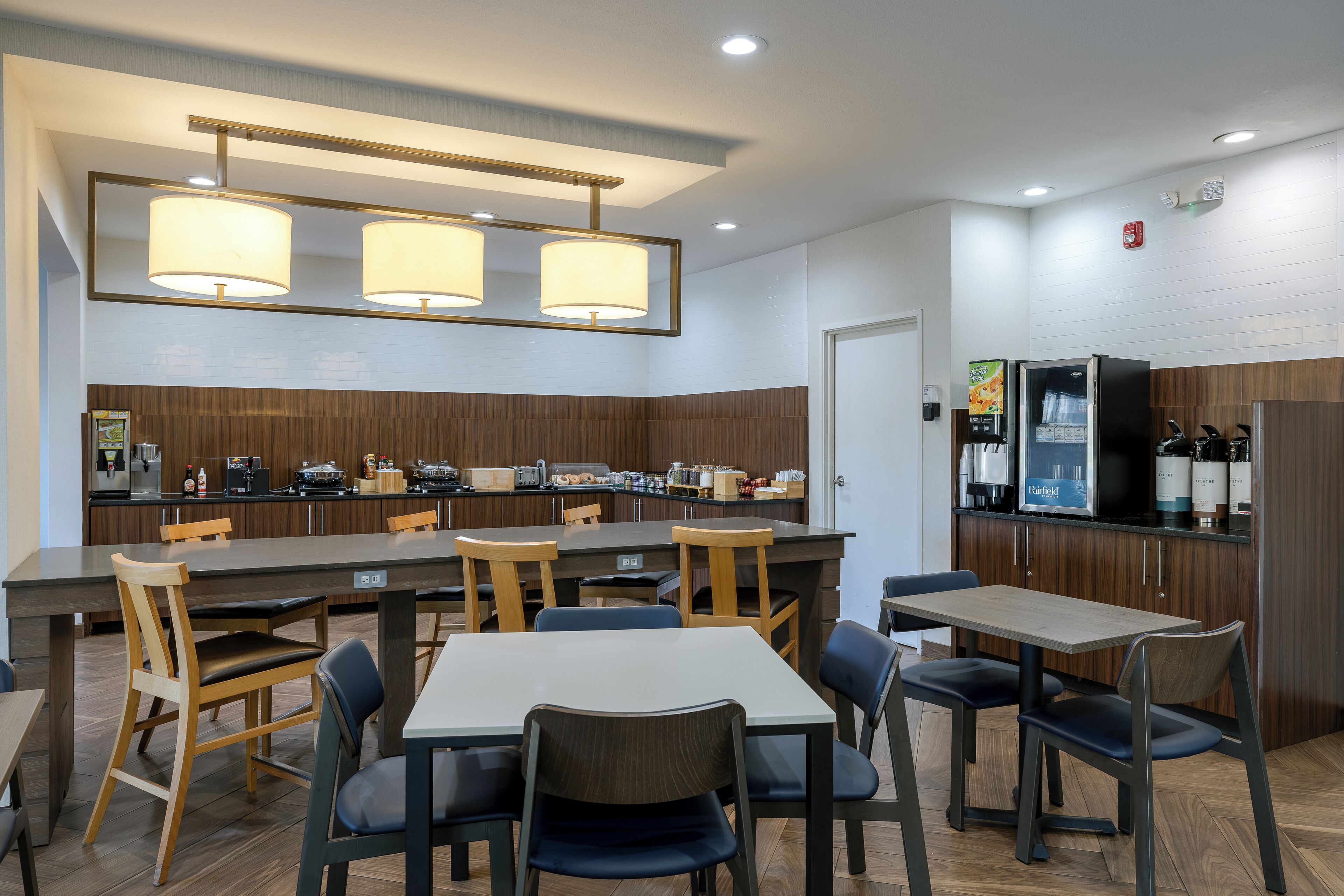 A modern kitchen with wooden cabinets, a central island, and a seating area with tables and chairs.