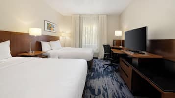 Habitación de hotel con dos camas, un escritorio, televisor y ventana con cortinas.