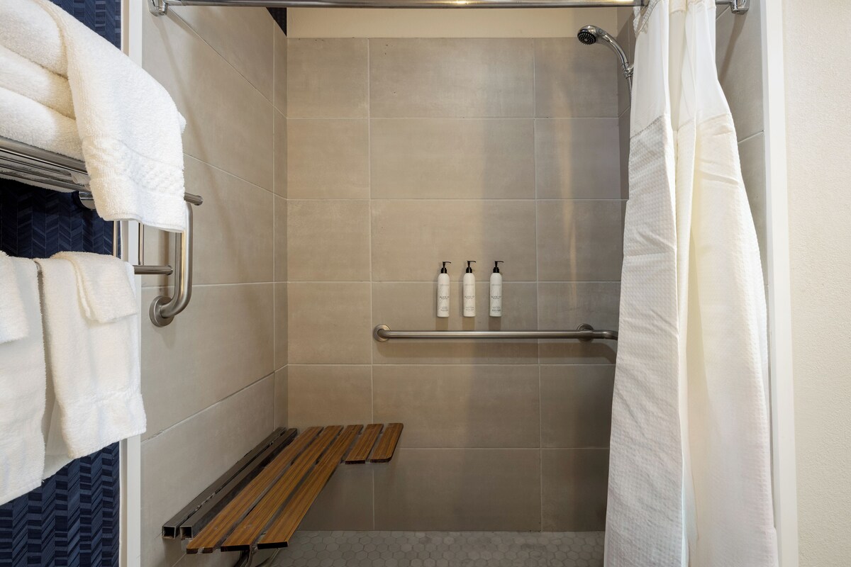 Una ducha con azulejos color beige, un banco de madera y dos botellas de champú en un estante.