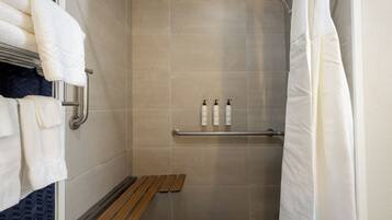 A shower with beige tiles, a wooden bench, and two bottles of shampoo on a shelf.