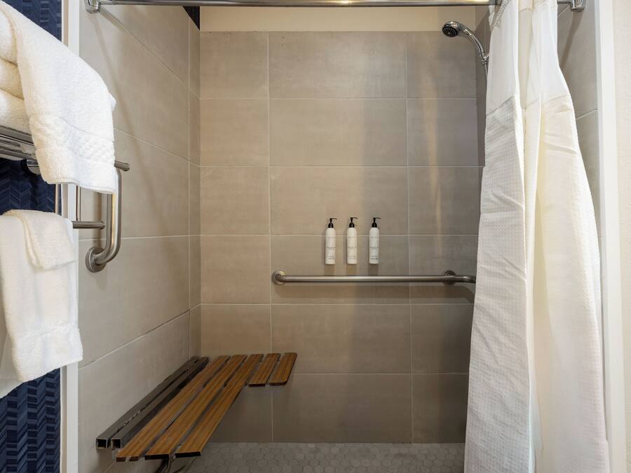 A shower with beige tiles, a wooden bench, and two bottles of shampoo on a shelf.