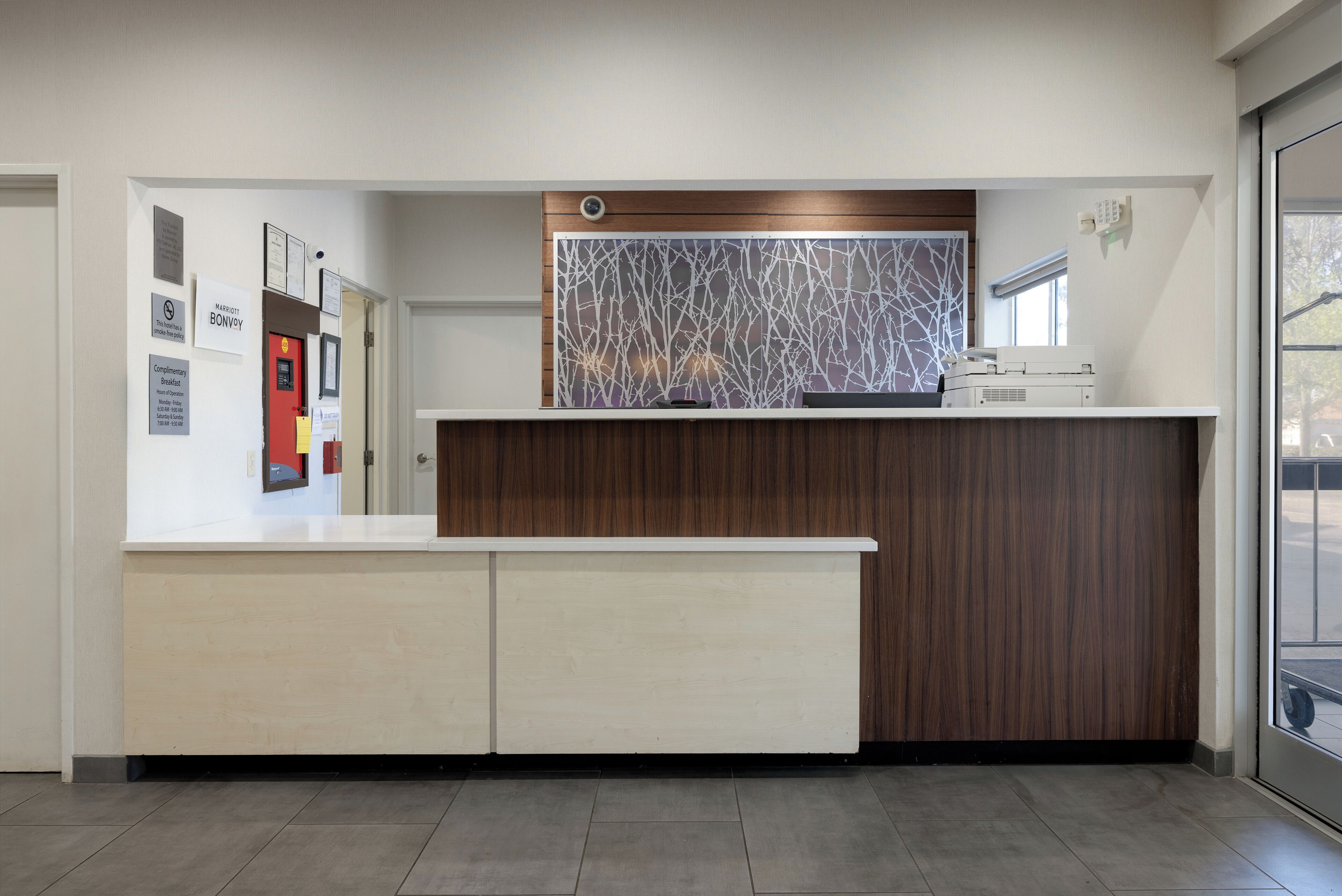 A reception desk with a modern design, a security camera above it, and a window to the right.