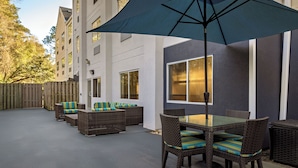 An outdoor patio area with wicker furniture, a glass table, and a large umbrella.