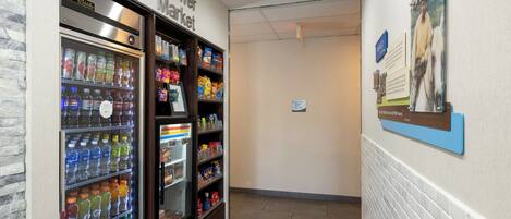 A corridor with a refrigerated beverage dispenser and snack shelves, a sign for the Corner Market, and a mounted informational poster.