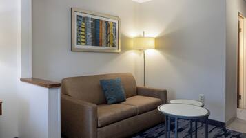 A hotel room with a brown sofa, a small round table, a lamp, and a framed picture on the wall.