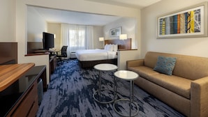 A hotel room with a bed, a sofa, a desk, a chair, and a TV.