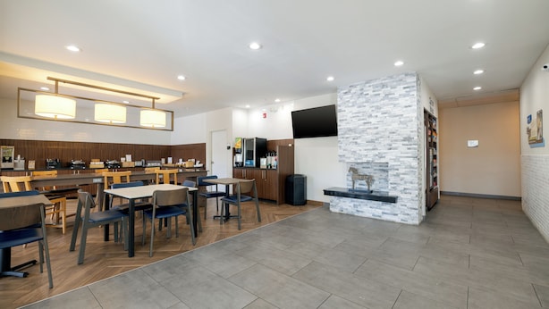 A modern restaurant with wooden tables and chairs, a stone accent wall, and a kitchen area in the background.