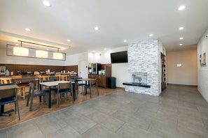 Un restaurante moderno con mesas y sillas de madera, una pared de acento de piedra y una zona de cocina al fondo.
