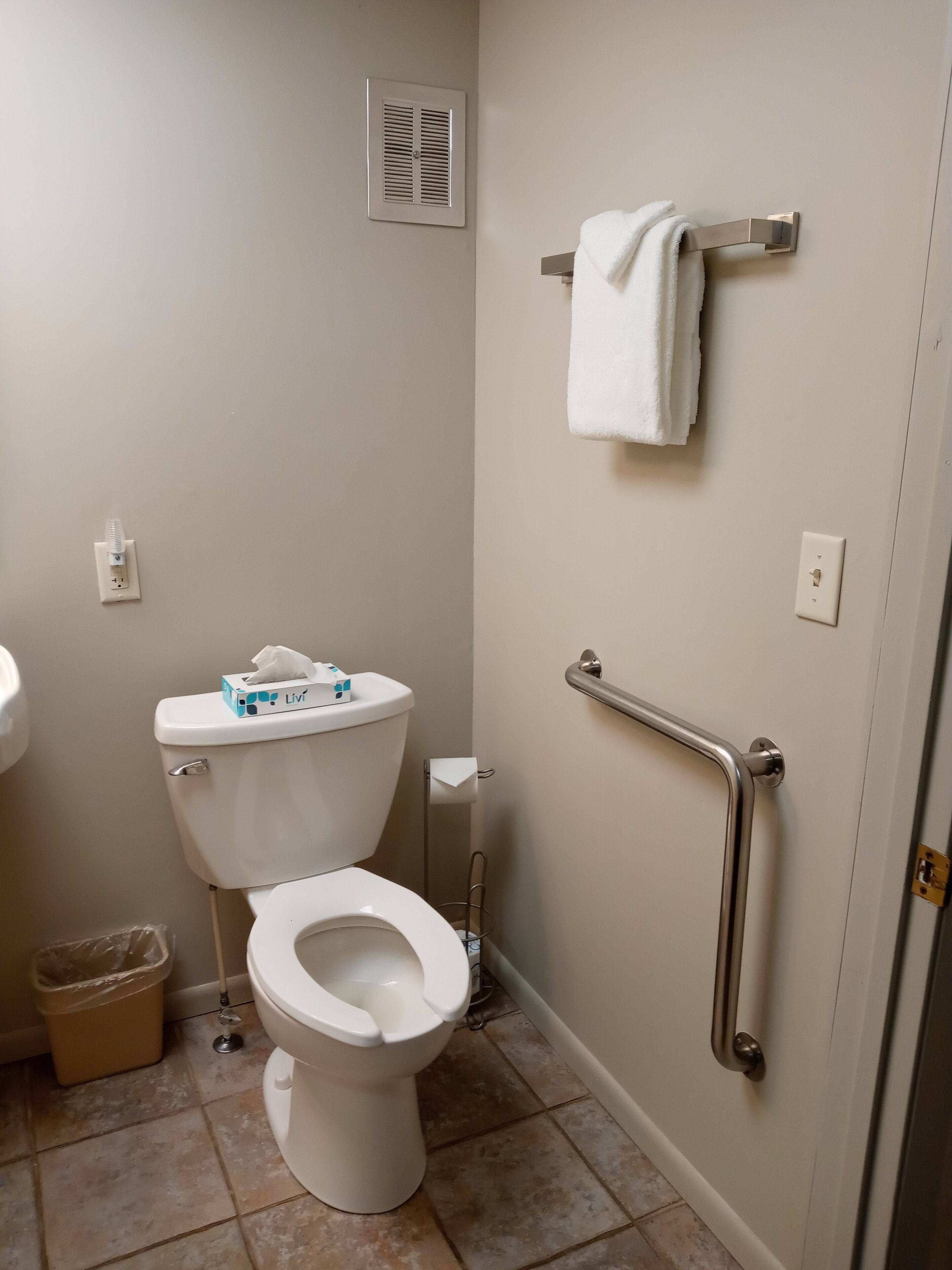 Une petite salle de bain comprenant des toilettes, une barre d’appui, un porte-serviettes et une poubelle.