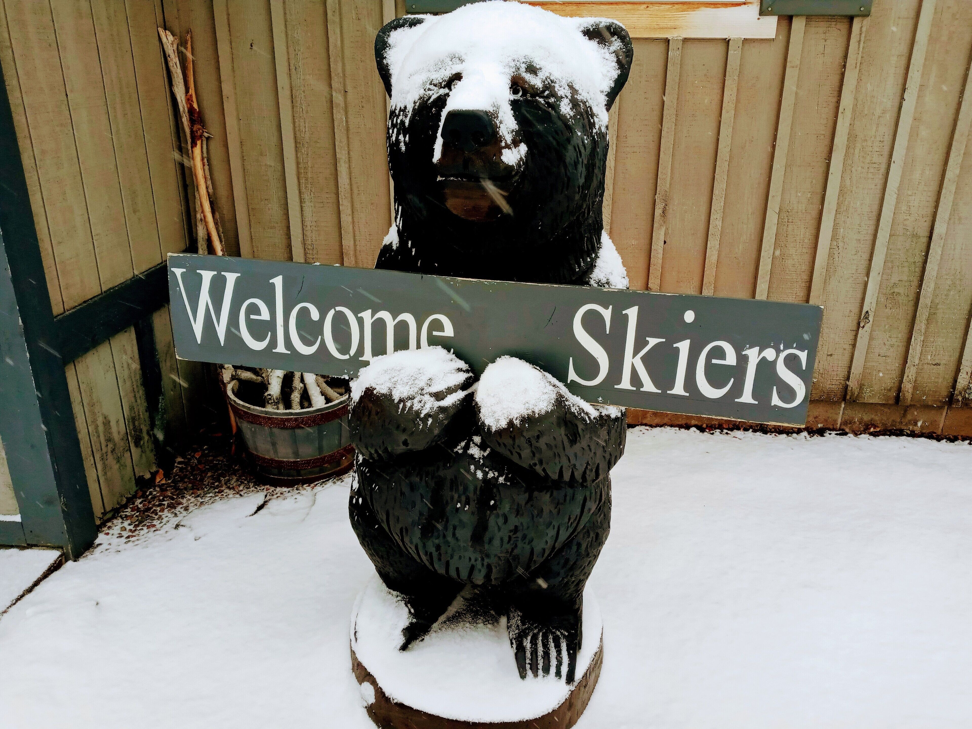 Un oso cubierto de nieve sosteniendo un letrero que dice 'Welcome Skiers'.
