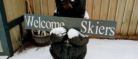Un ours couvert de neige tenant une pancarte sur laquelle on peut lire : « Bienvenue aux skieurs ».