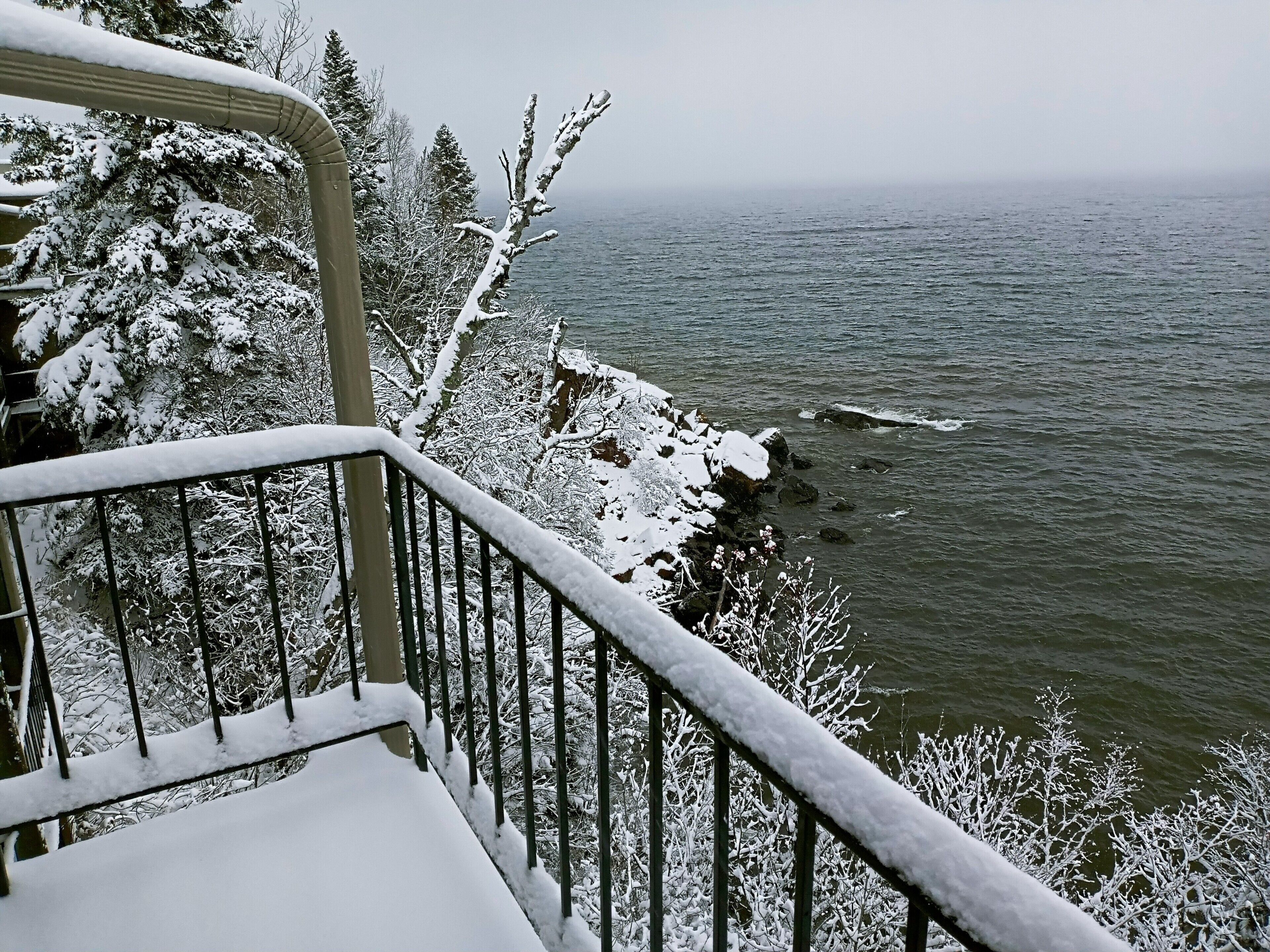A snow-covered balcony with a view of a lake and trees.