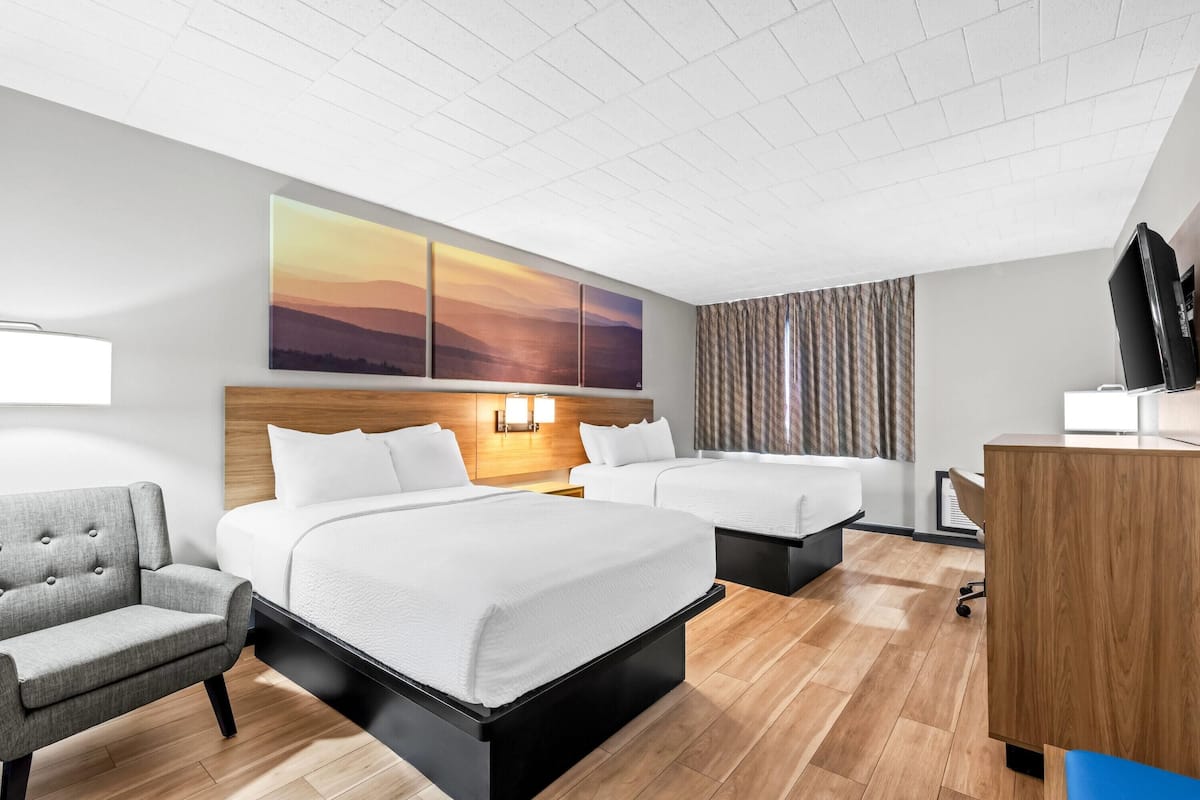 A hotel room with two beds, a desk, a chair, and a large painting on the wall.