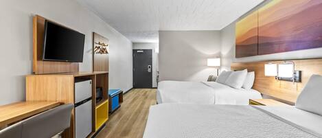 A hotel room with a bed, a desk, a television, a mini-fridge, and a painting on the wall.