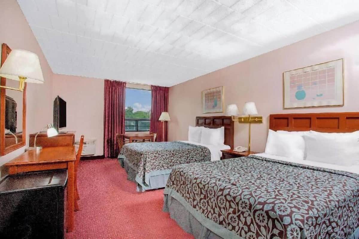 A hotel room with two beds, a desk, a chair, a window with curtains, and a ceiling with a grid pattern.