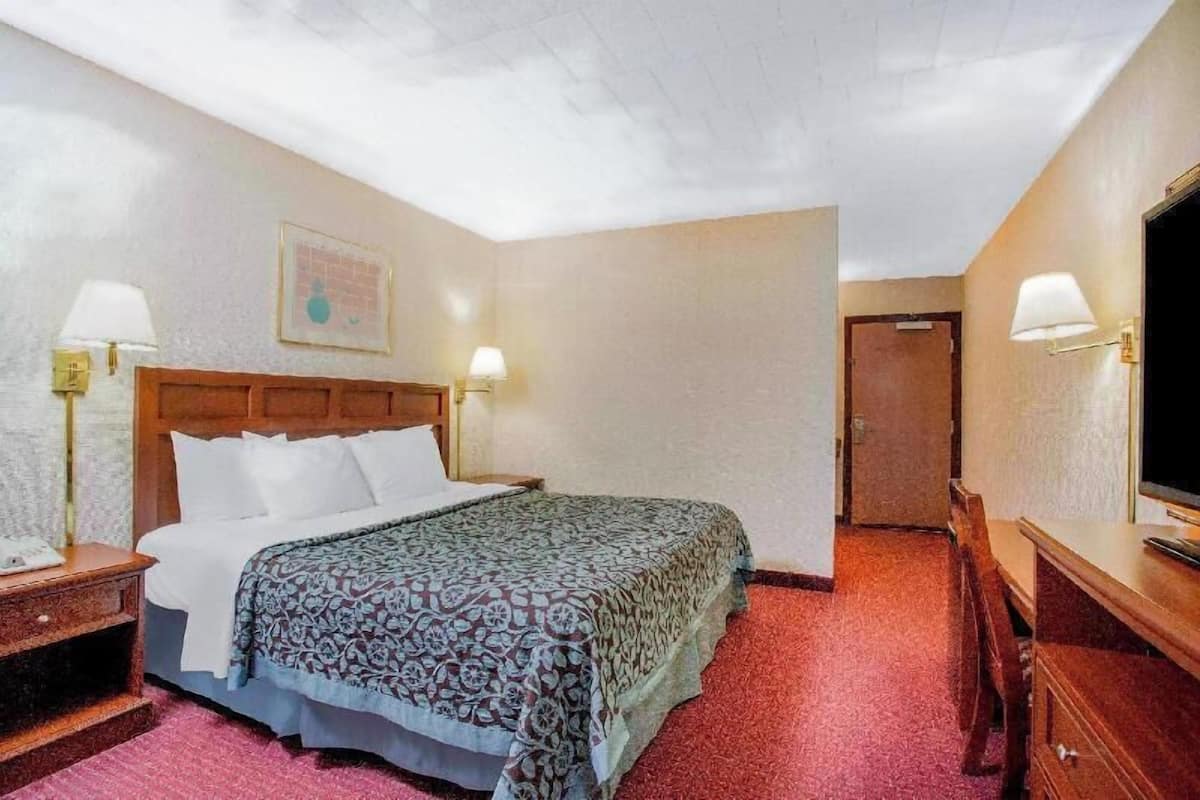 A hotel room with a bed, bedside lamps, a television, a wooden headboard, and a door.